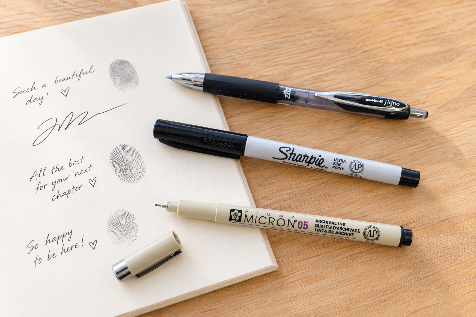Three black pens for guest book signing: Uni-ball Signo, Sharpie Ultra Fine Point, and Sakura Pigma Micron 05.