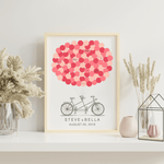 Framed tandem bike signature balloon guest book displayed at a wedding reception table with flowers and candles