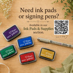 Promotional graphic for Pure Palette ink pads and signing pens on a wooden surface, showing five ink pads in purple, blue, green, red, and gold, a Micron DB pen, and text inviting shoppers to the Ink Pads & Supplies section with a QR code.